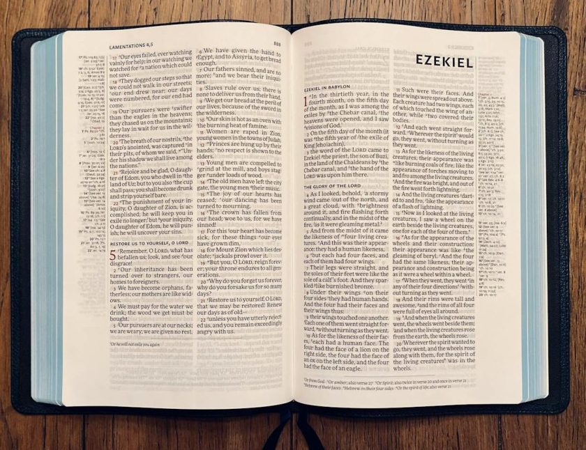 An open Bible on a wooden surface, displaying text from the books of Lamentations and Ezekiel, with a dark leather cover and blue page edges.